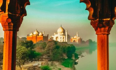 Taj Mahal seen through an intricately carved red stone archway during early morning light.