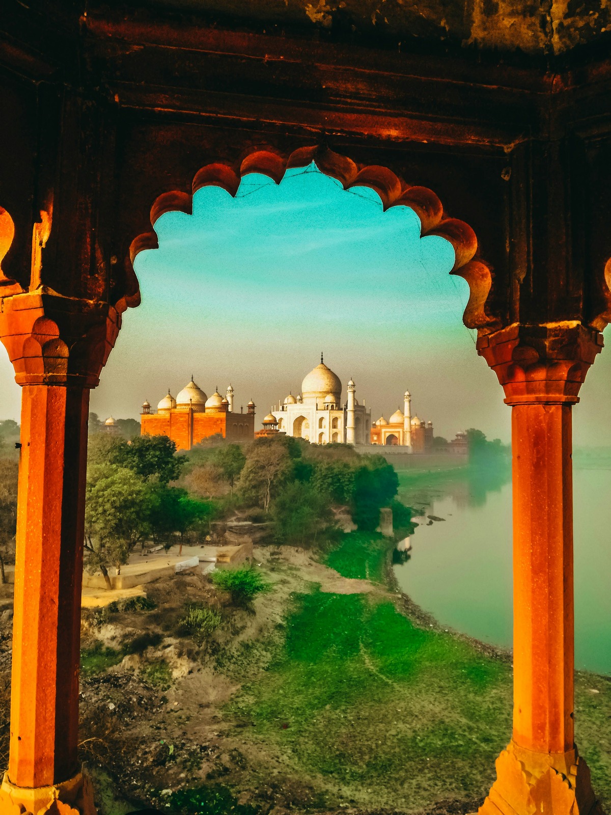 Taj Mahal seen through an intricately carved red stone archway during early morning light.