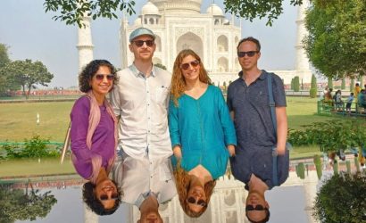 Four tourists enjoy a Taj Mahal tour from New Delhi, posing in front of the iconic monument with their reflections in a calm pool of water.